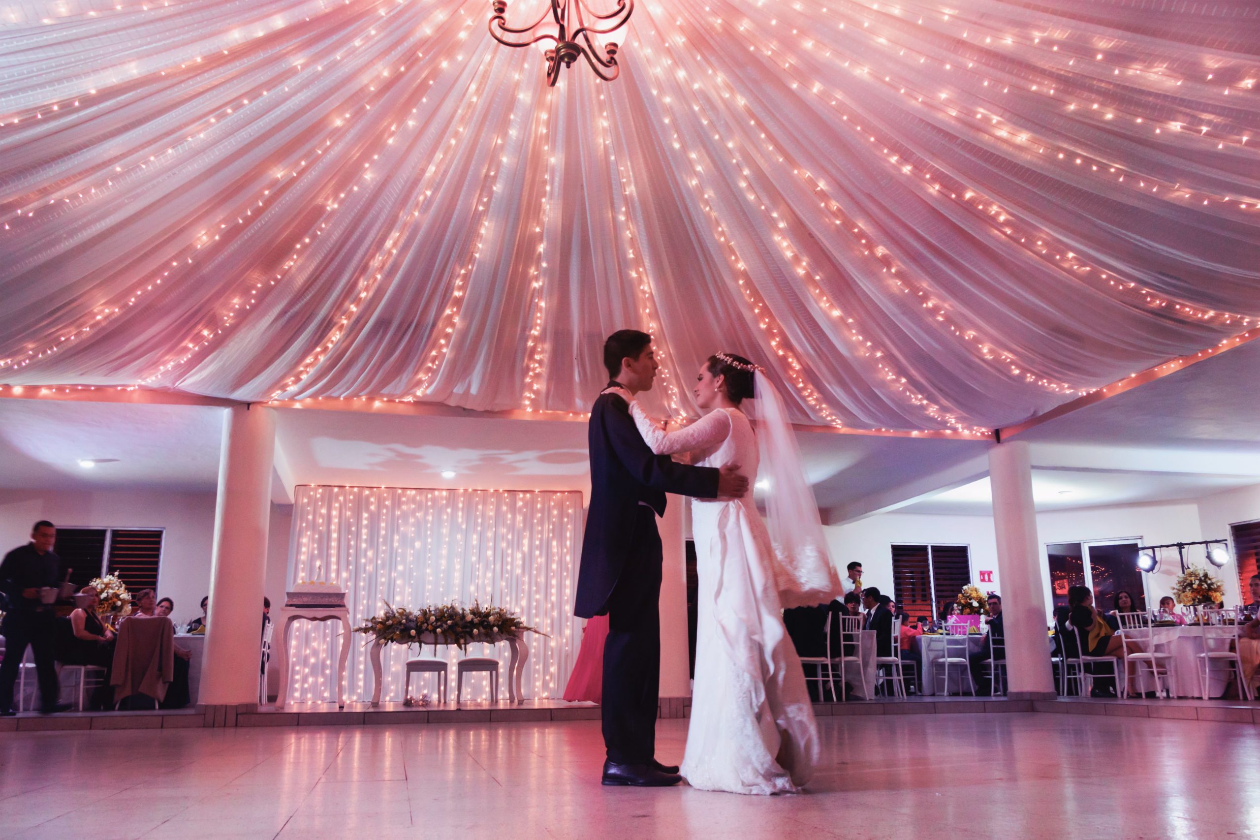 pareja de novios bailando en un salón bajo una carpa rosada y luces que iluminan todo