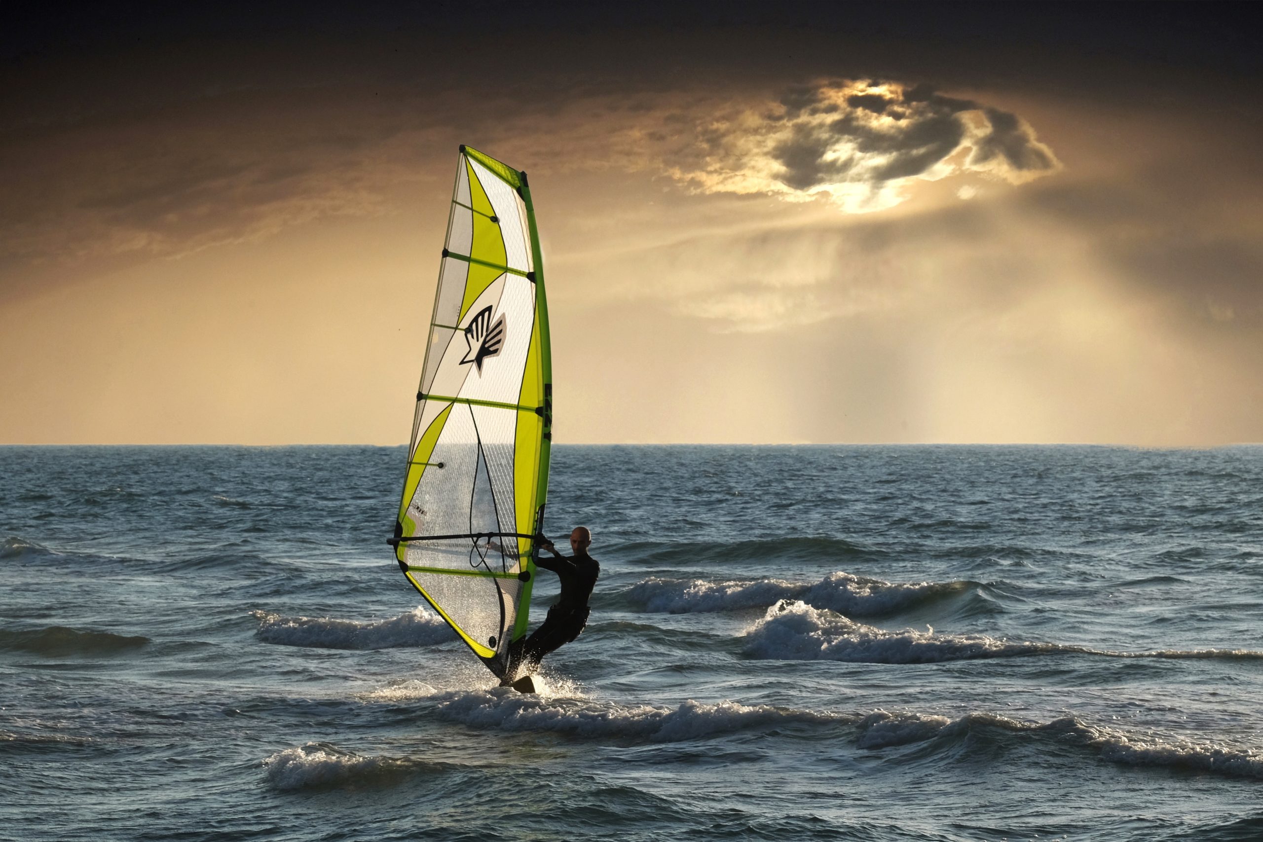 una tabla de windsurf en medio del mar, pasando de forma suave con el atardecer de fondo